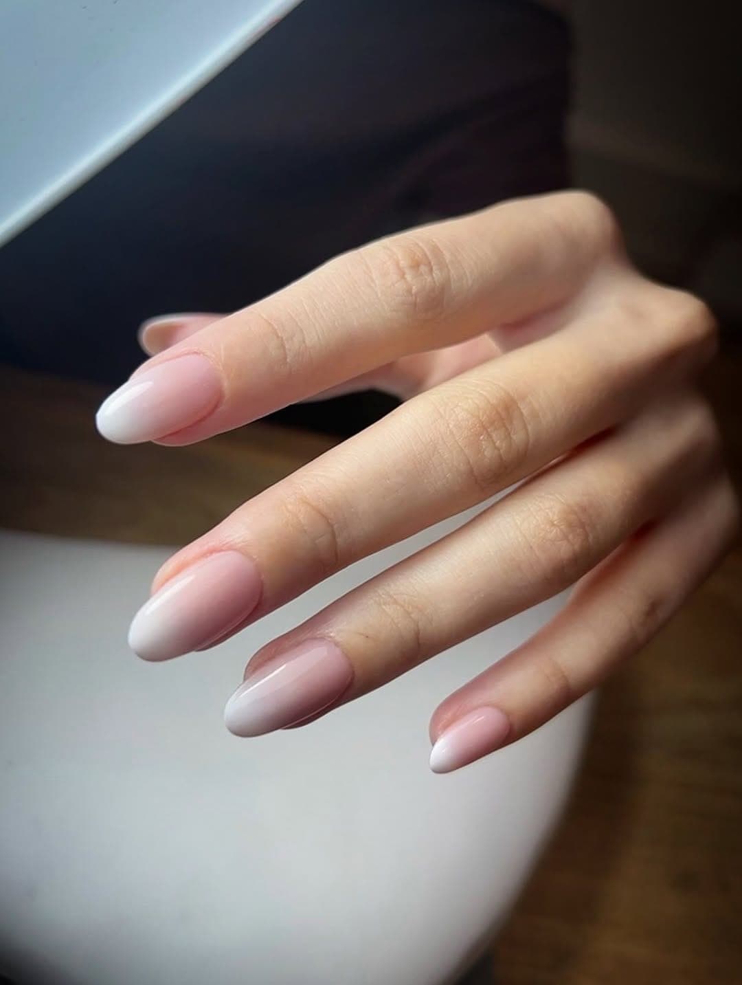 Main aux ongles amande, dégradé rose vers le blanc, posé si fin qu’on distingue l’ongle naturel.